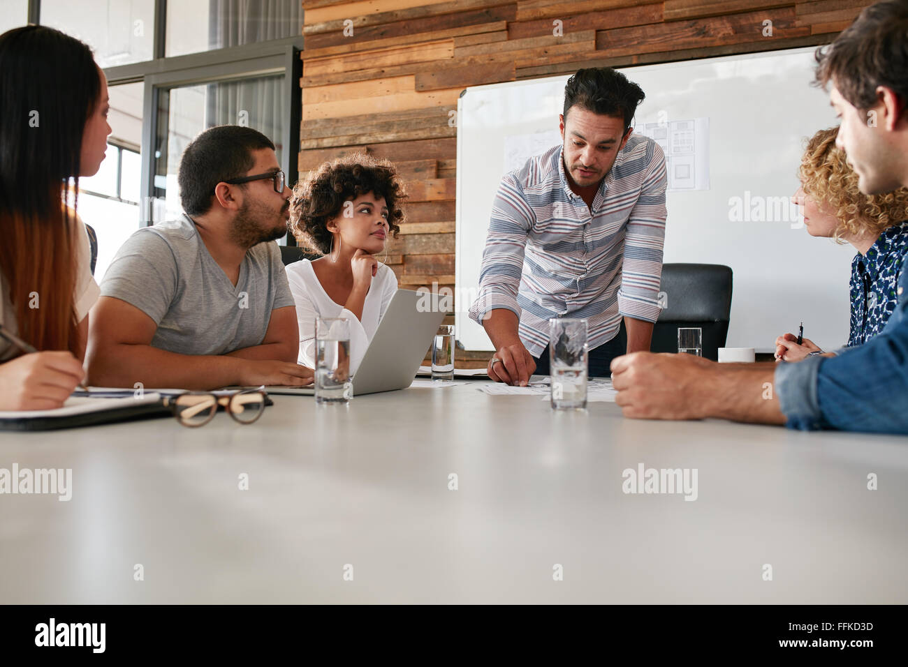 Giovane team aziendale nel corso di una riunione per discutere i progressi dell'azienda. I creativi professionisti seduti attorno a un tavolo in ufficio. Foto Stock