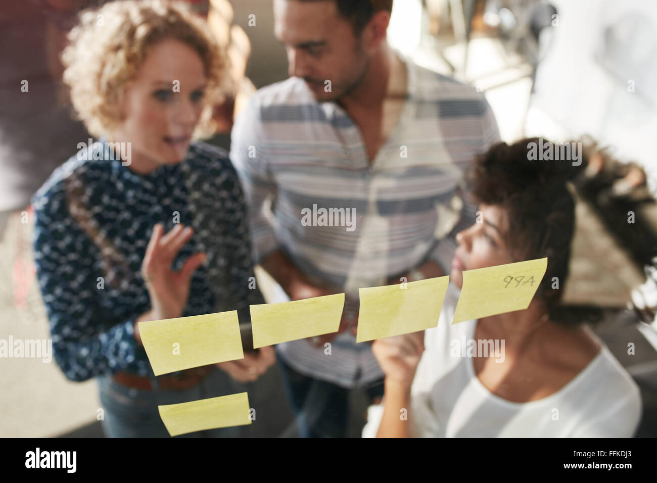 Tre persone di affari avente una riunione in ufficio. Essi sono in piedi nella parte anteriore della parete di vetro con post-it e discutere. Foto Stock