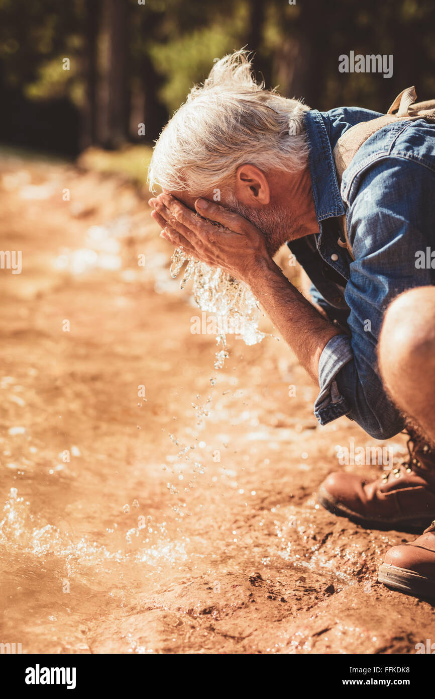 Lato ritratto di un uomo anziano lavando il suo volto nel lago. Maschio maturo escursionista getting fresco con acqua di lago. Foto Stock