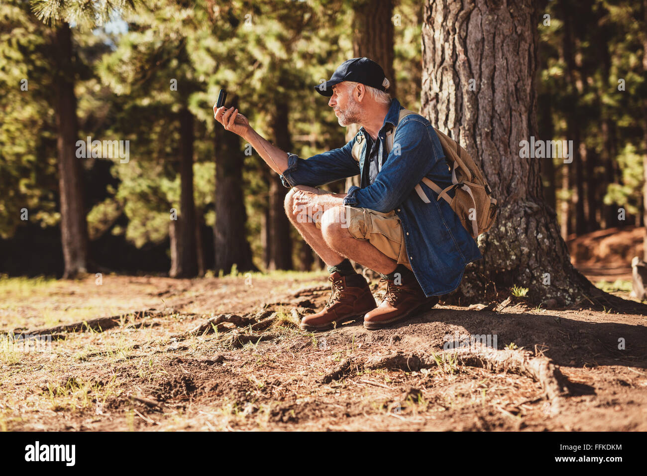 Uomo maturo si ferma per controllare la sua posizione utilizzando una bussola mentre fuori su escursione nella foresta. escursionista maschile seduto da un albero in fores Foto Stock