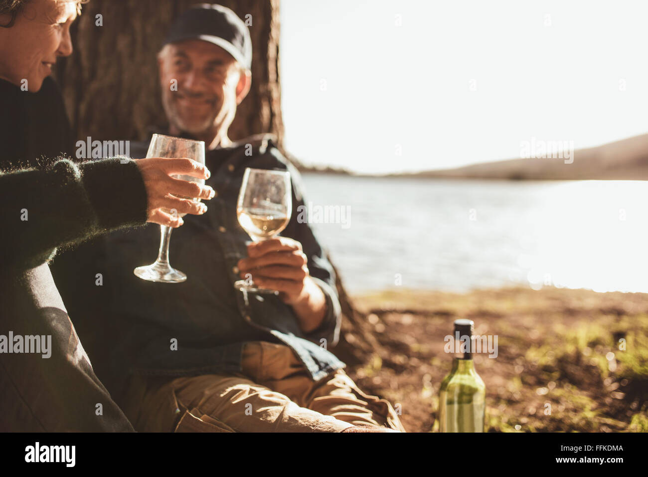 Close up ritratto della coppia senior bere il vino durante il campeggio vicino a un lago. Concentrarsi sulle mani tenendo un bicchiere di vino. Foto Stock