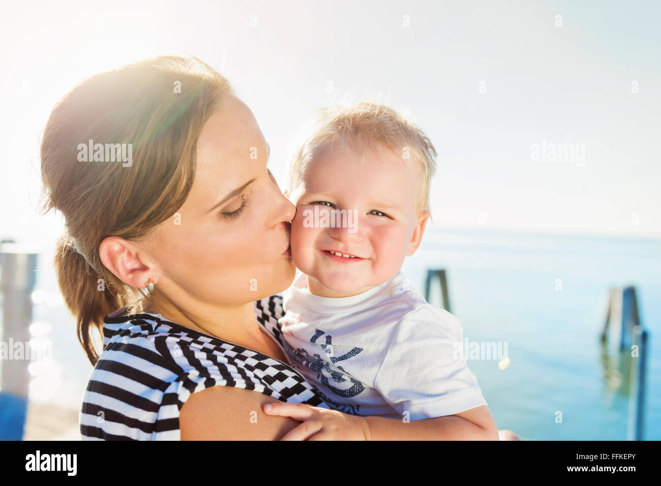 Madre baciare il suo ragazzo, estivo soleggiato dall'acqua Foto Stock