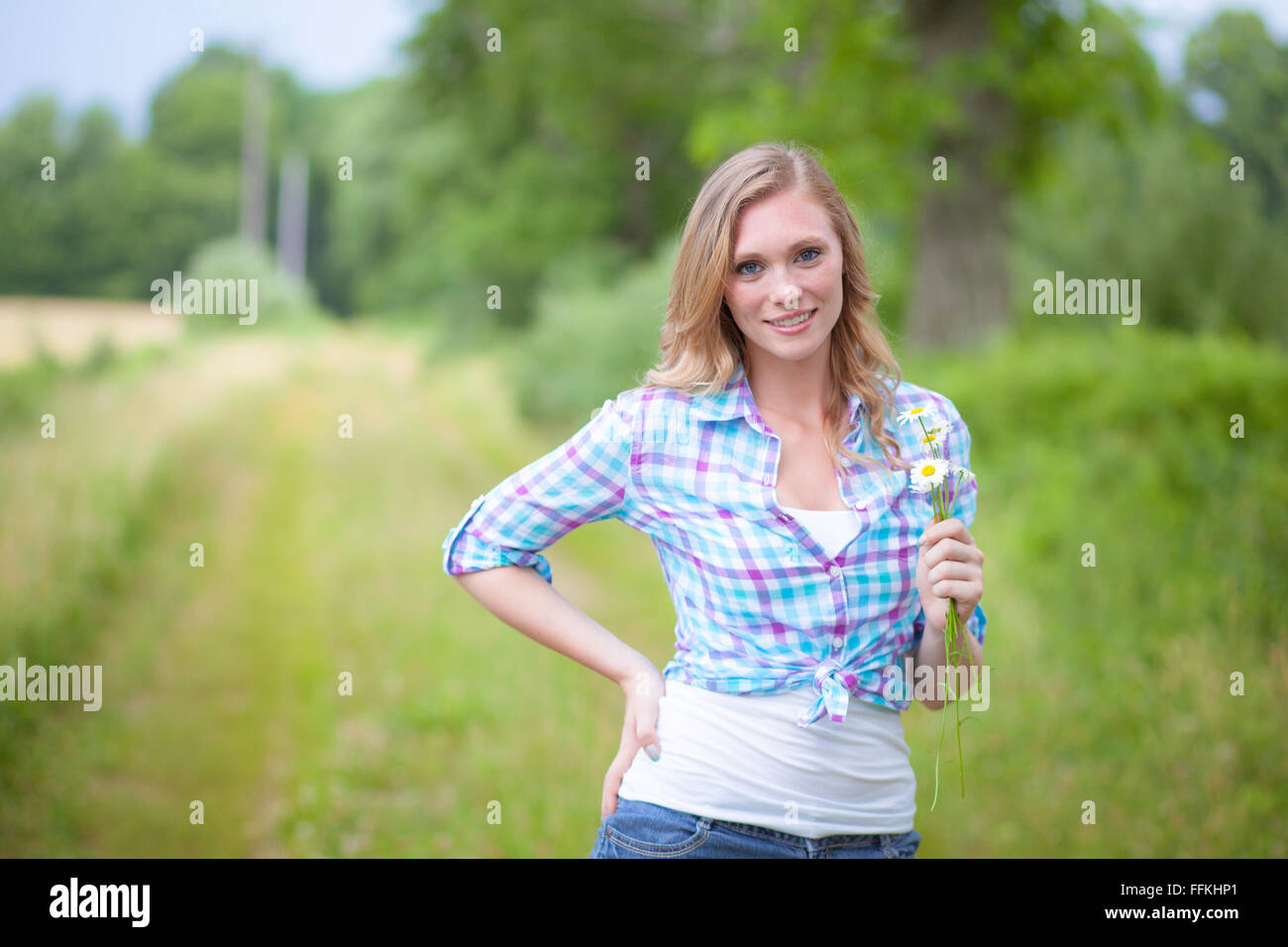 Sorridente bella donna bionda azienda fiore e in piedi su una strada di campagna Foto Stock