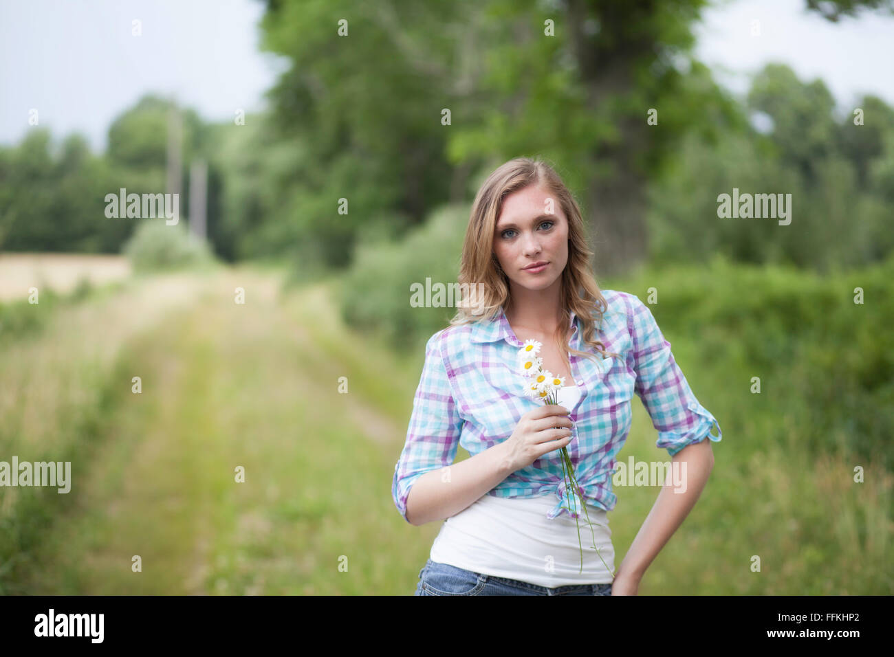 Bella donna bionda sulla strada di un paese tenendo i fiori Foto Stock