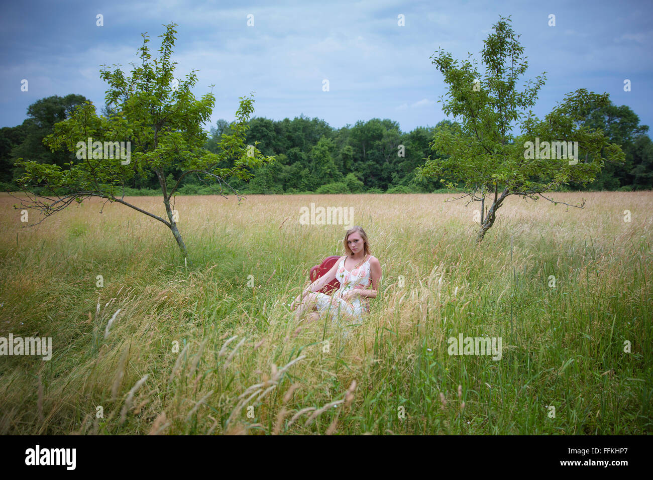 Bella donna bionda seduto in una sedia rossa in un campo di erba alta Foto Stock