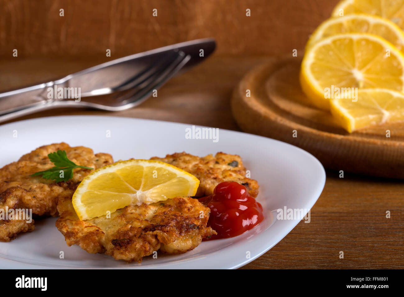 Ketchup con la Wiener Schnitzel e le fette di limone sulla piastra bianca con sfondo di legno Foto Stock