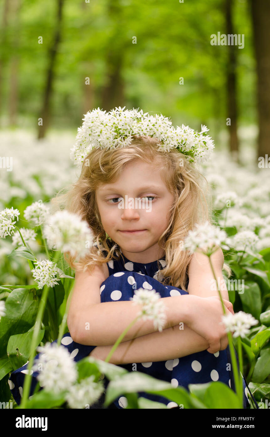 Adorabile bionda ragazza seduta tra i fiori bianchi nel verde dei boschi Foto Stock