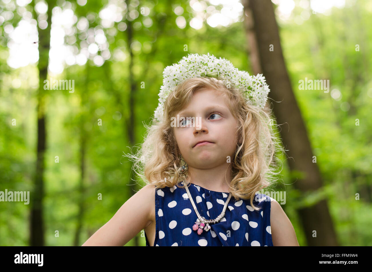 Adorabile ragazza bionda con fiori di colore bianco sopra la testa nel verde dei boschi Foto Stock