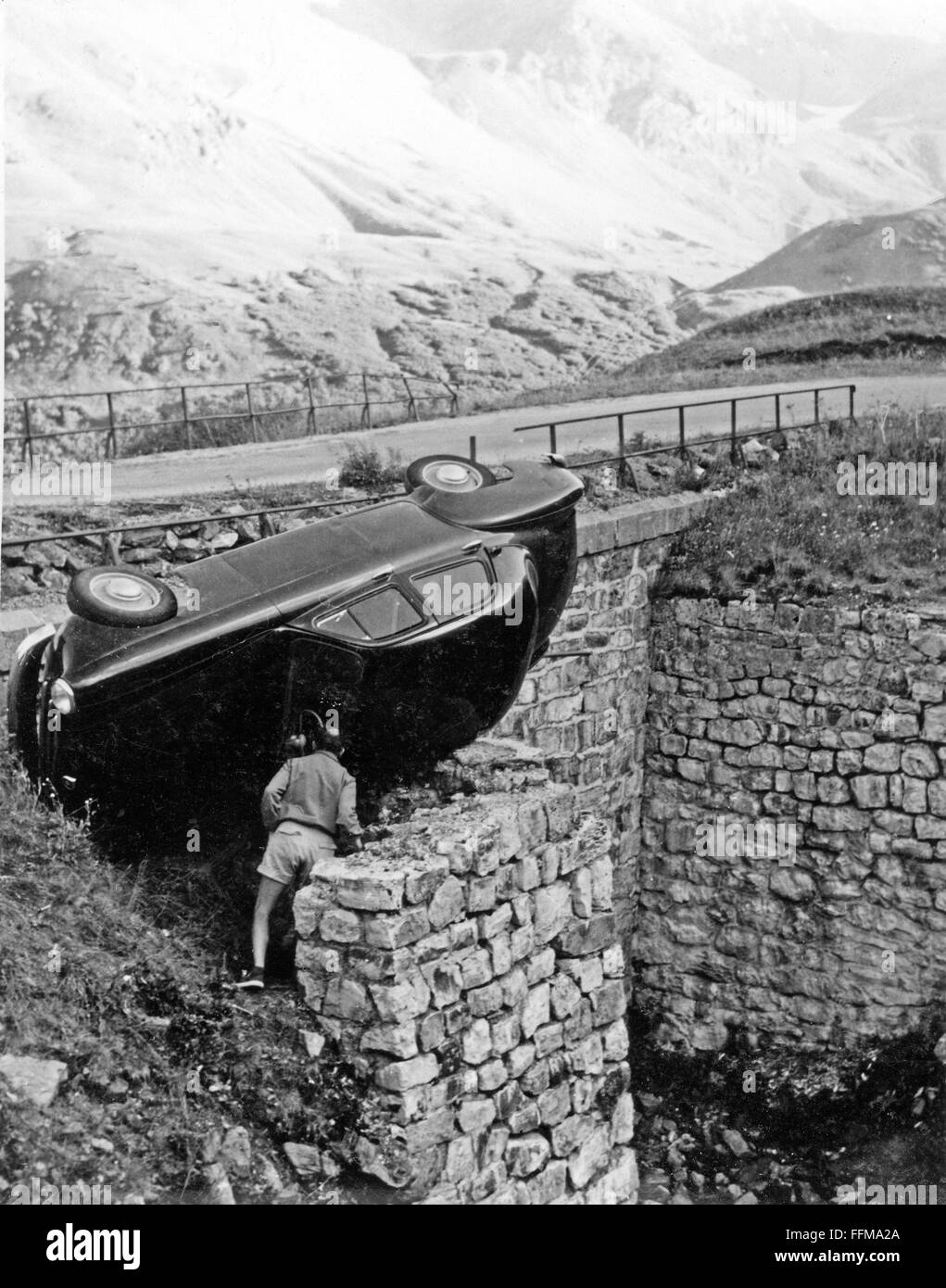 Un uomo ispeziona un auto si è schiantato su una grande strada alpina in Svizzera negli anni cinquanta. Foto Stock