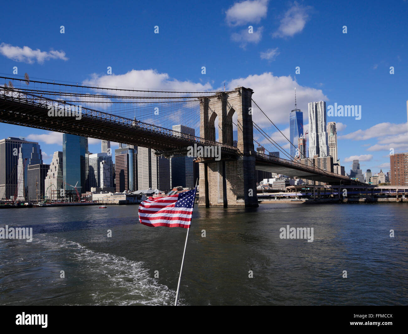 Stelle e Strisce vola al di sotto del ponte di Brooklyn con la parte inferiore di Manhattan in background, New York, Stati Uniti d'America. Foto Stock