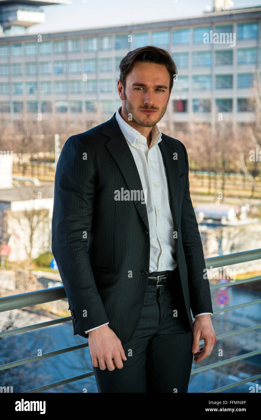 Mezzo corpo Ritratto di giovane ed elegante uomo che indossa business suit, in piedi contro il metallo corrimano per esterno Foto Stock