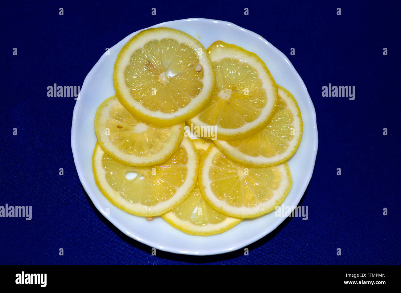 Mature limone tagliato in segmenti su una piastra, un limone, frutto maturo, giallo su una piastra, una piastra bianca, uno sfondo blu Foto Stock