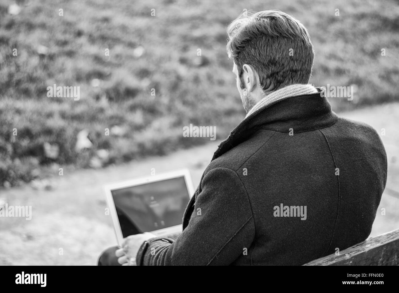 Bello ed elegante imprenditore seduto su una panca in legno per lavorare in esterno in un parco urbano di digitare le informazioni sul suo computer portatile comp Foto Stock
