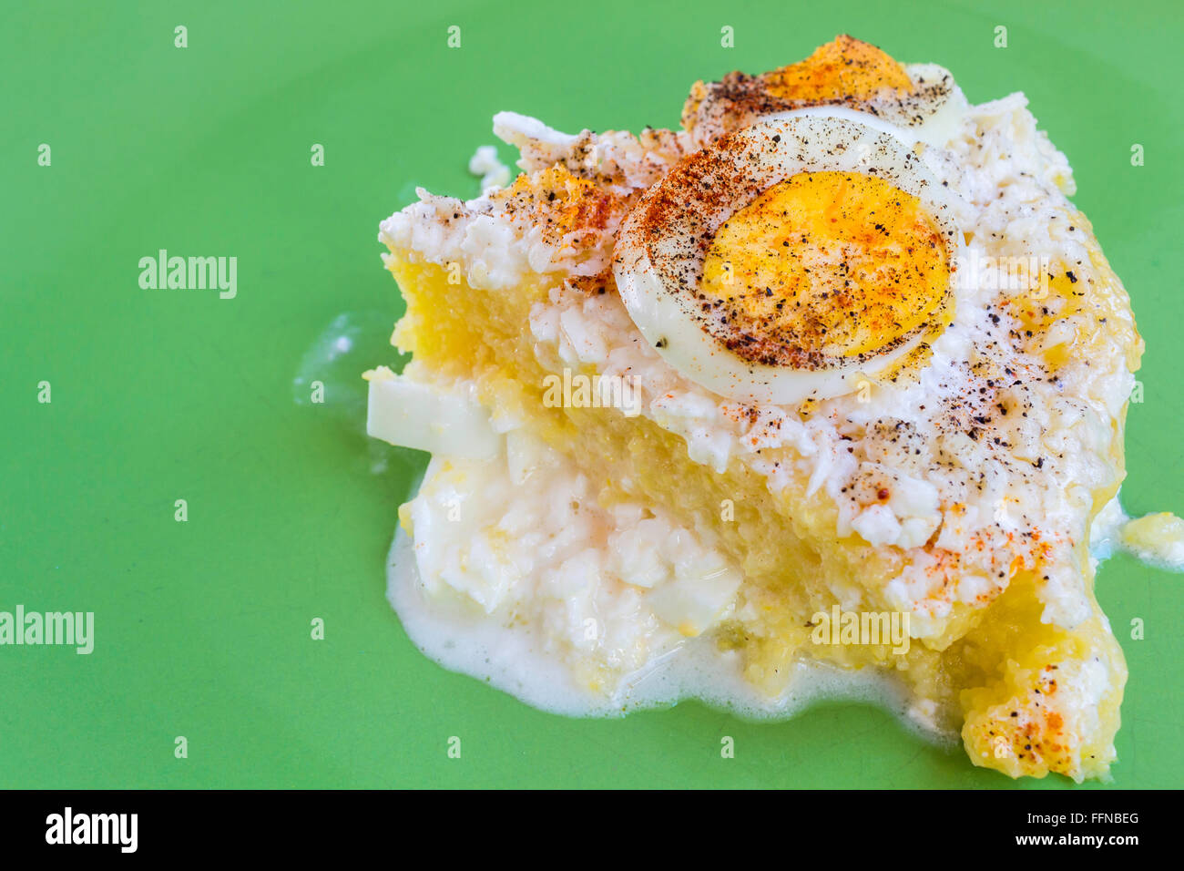 Polenta (mamaliga) slice con uova sode, la panna acida e il formaggio di capra su una piastra verde Foto Stock