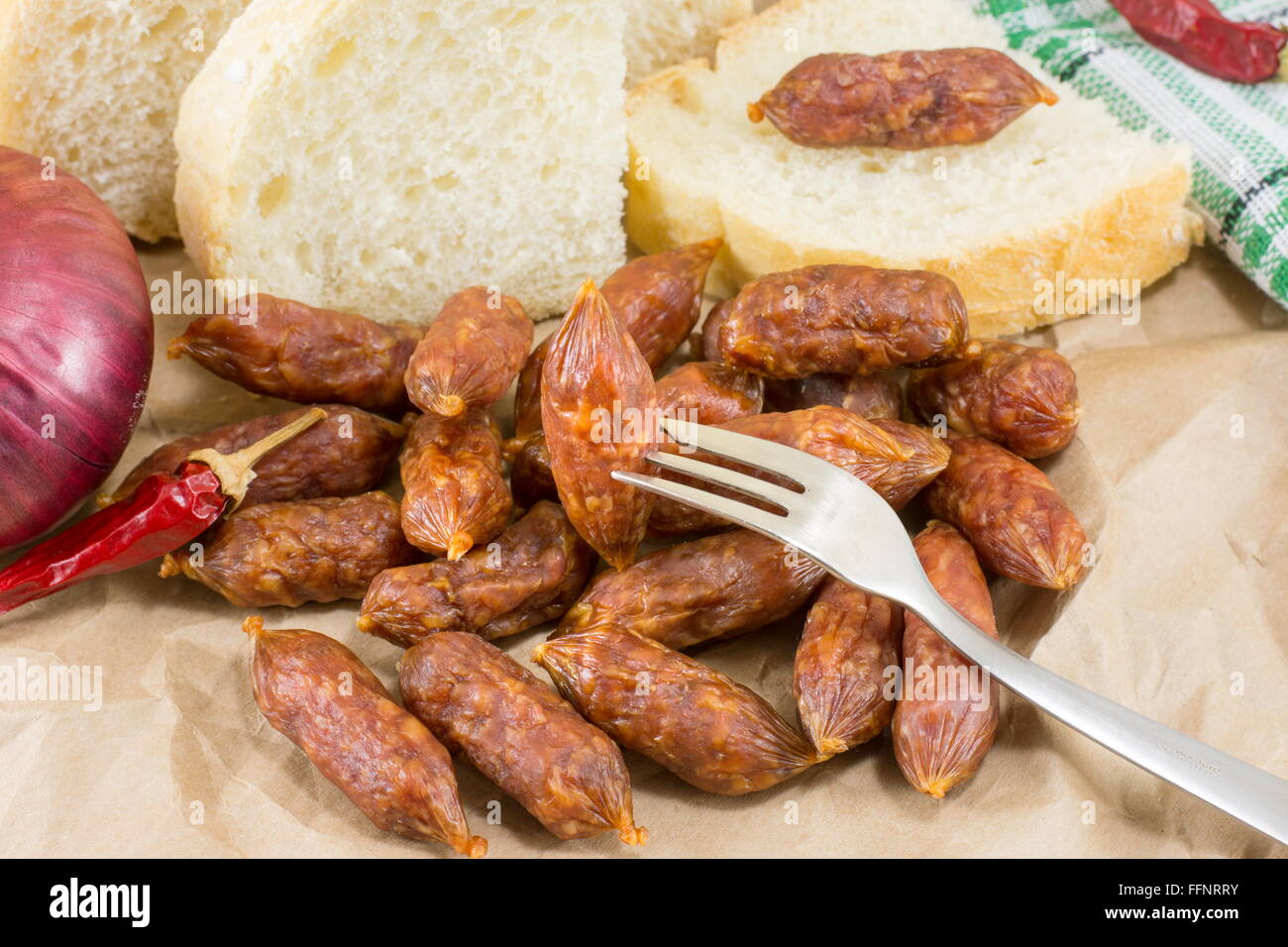 Piccole salsicce fatte in casa su un pezzo di carta marrone con pane verdure e posate Foto Stock