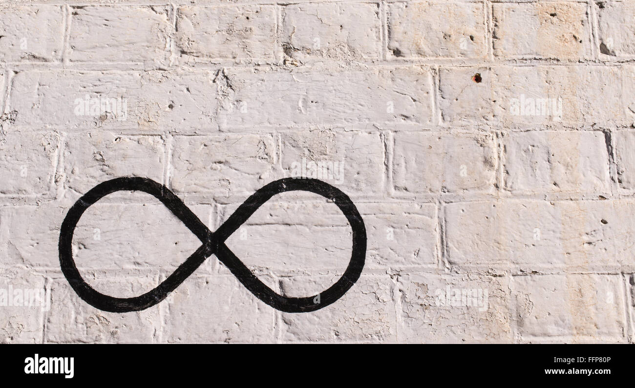 Il simbolo di infinito disegnato in nero su un muro di mattoni dipinto in bianco. Foto Stock