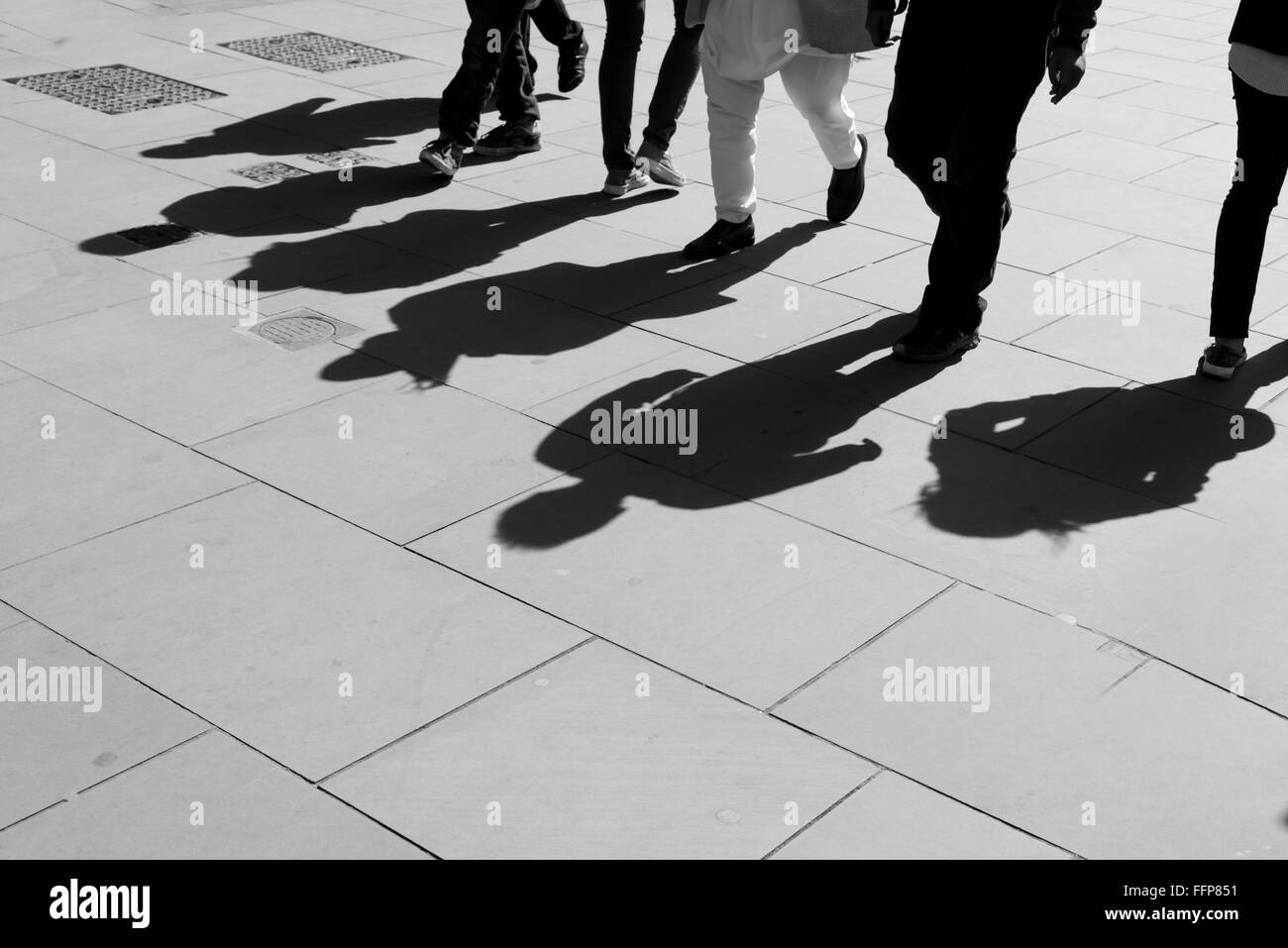 Ombre di sei piedi pedoni proiettata sul marciapiede. In bianco e nero. Foto Stock