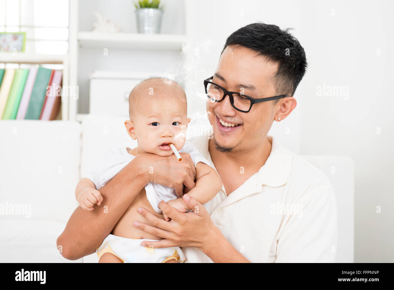 Famiglia asiatica a casa. Bad padre dando sigaretta per bambino. Con la sigaretta accesa e il fumo. Uno stile di vita poco salutare o smettere di fumare con Foto Stock