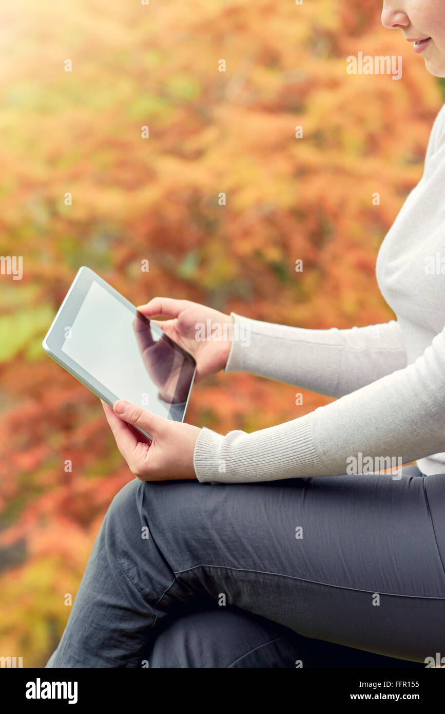 Donna che mantiene un tablet PC in autunno park. Composta verticalmente e cross-immagine elaborata con tonificazione del colore Foto Stock