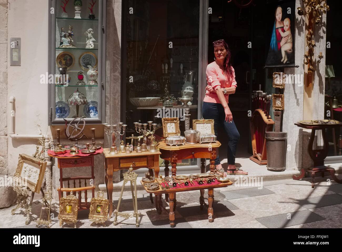 Una signora negoziante fuma una sigaretta in attesa per i clienti al negozio di antiquariato appena fuori la high street a Taormina, Sici Foto Stock
