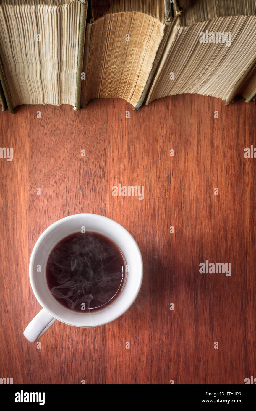 Tazza di caffè in piedi accanto alla pila di libri antichi Foto Stock