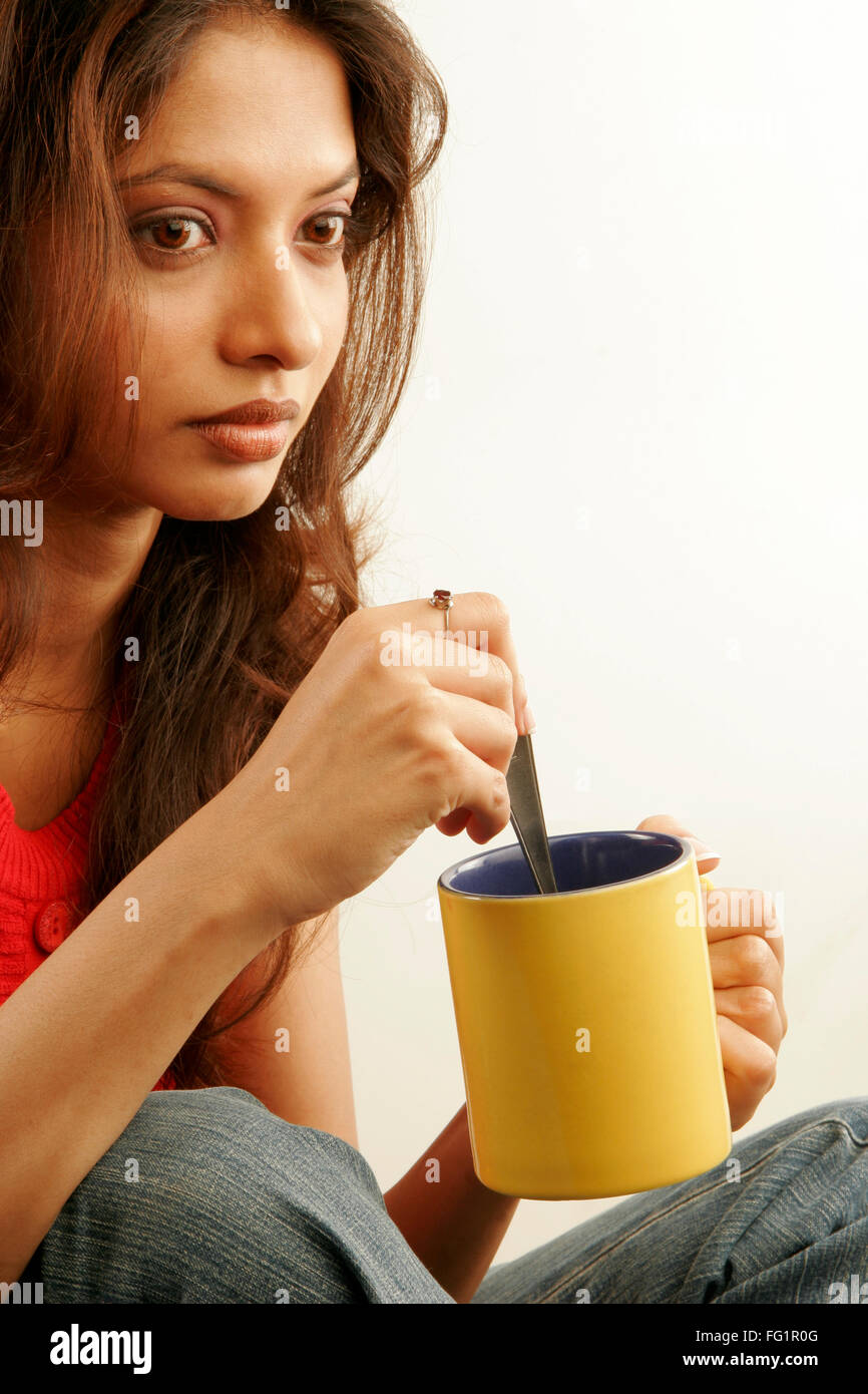 South Asian indiano ragazza adolescente indossando rosso top senza maniche assorto nei suoi pensieri holding giallo mug signor#686G Foto Stock