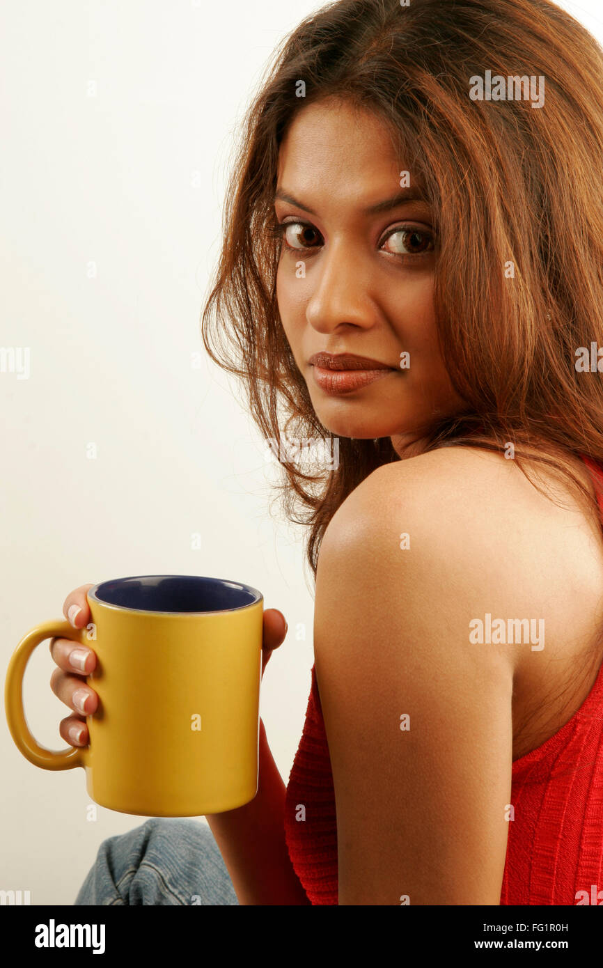 South Asian indiano ragazza adolescente indossando rosso top senza maniche godendo di caffè nella tazza giallo signor#686G Foto Stock