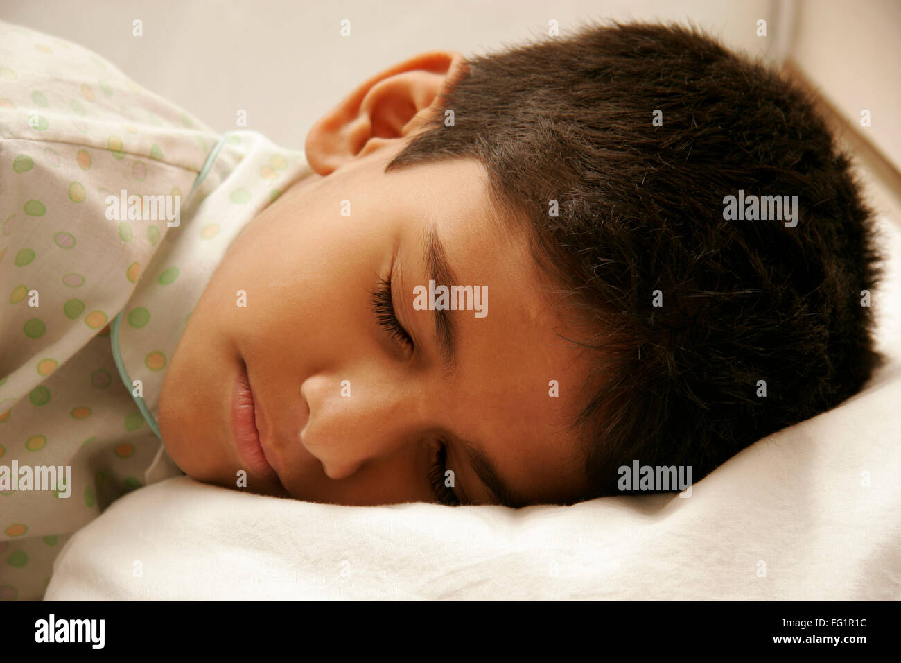 South Asian Indian 8 anni vecchio ragazzo indossa indumenti da letto bianco con luce punti di colore avente suono addormentato sul letto signor#686D Foto Stock
