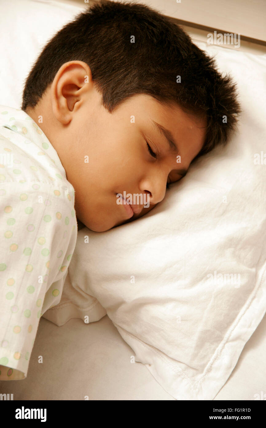 South Asian Indian 8 anni vecchio ragazzo indossa indumenti da letto bianco con luce punti di colore avente suono addormentato sul letto signor#686D Foto Stock