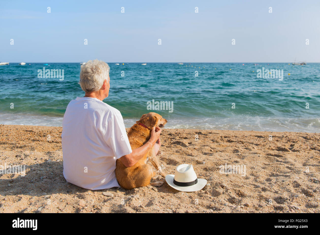 Senior Uomo con cane in abito bianco seduto alla spiaggia Foto Stock