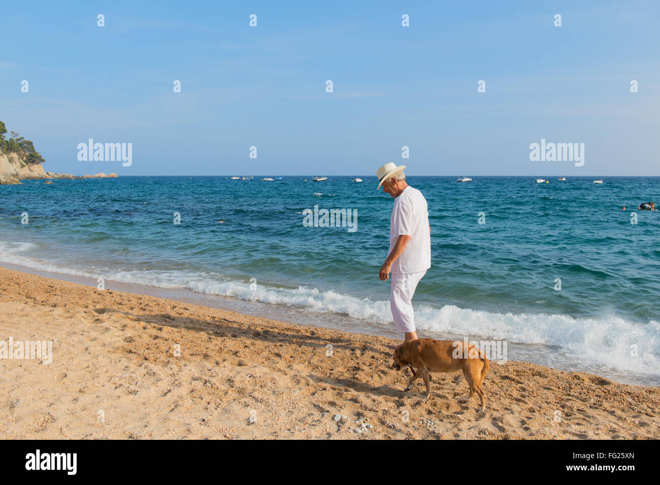 Senior Uomo con cane in abito bianco a piedi la spiaggia Foto Stock