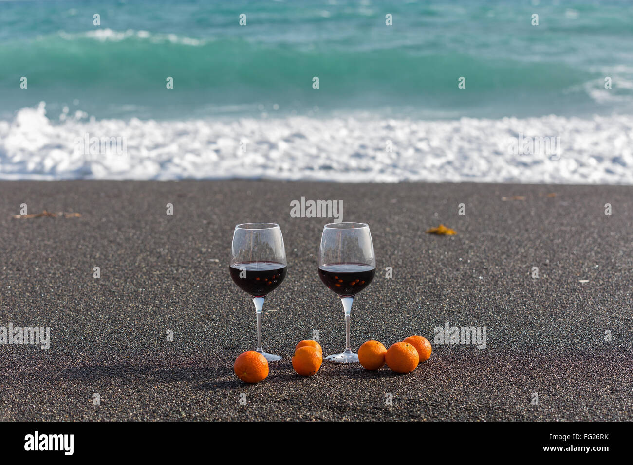 Due bicchieri di vino rosso e i tangerini sulla sabbia di mare Foto Stock