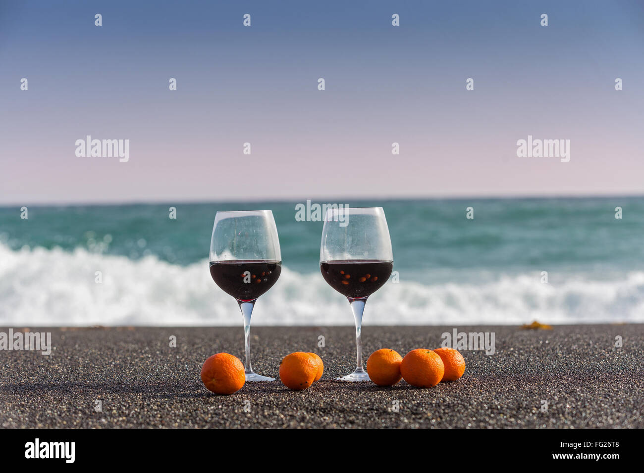 Due bicchieri di vino rosso e i tangerini sulla sabbia di mare Foto Stock