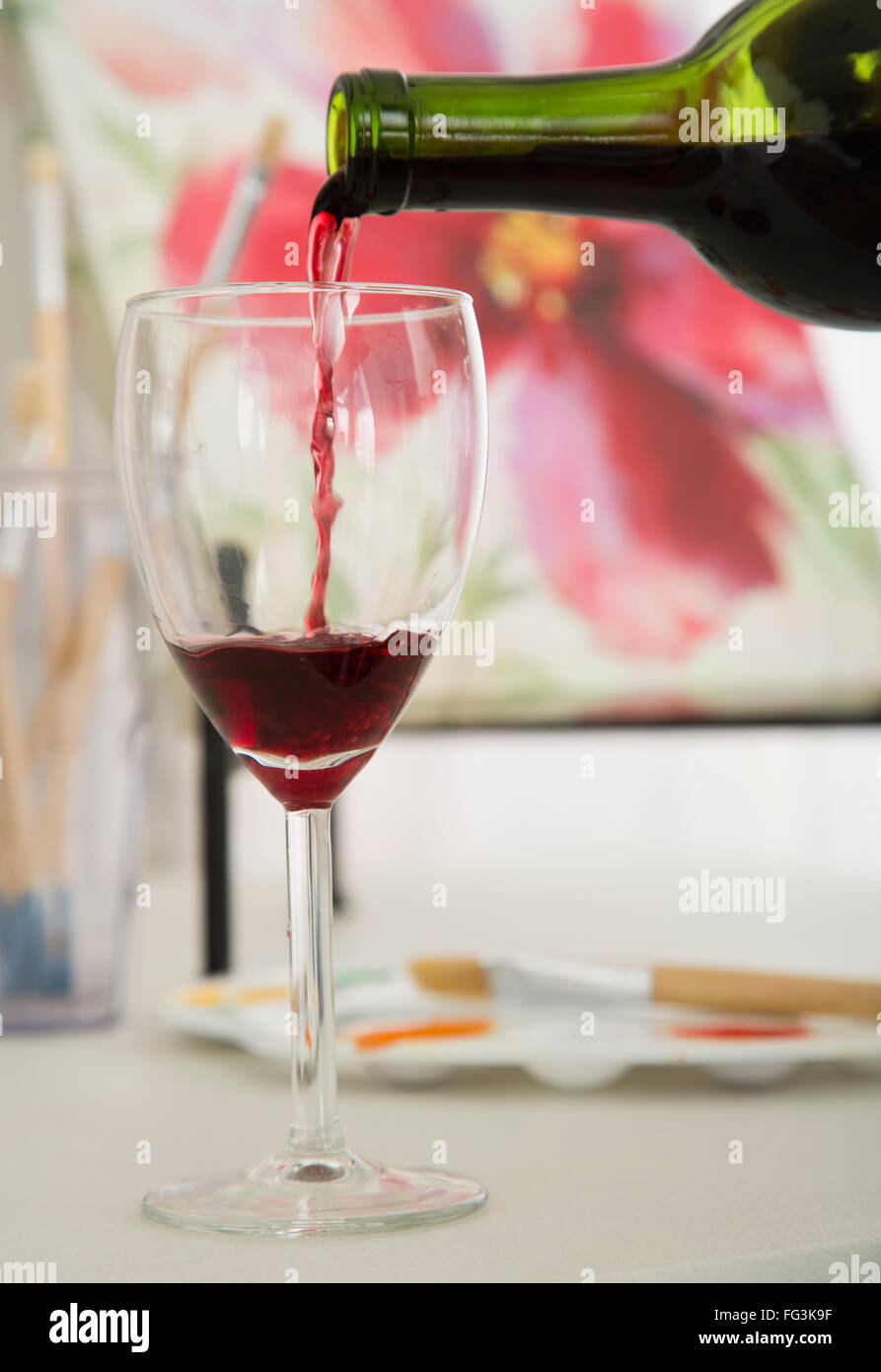 Vino rosso versando in vetro del vino con la pittura in background Foto Stock