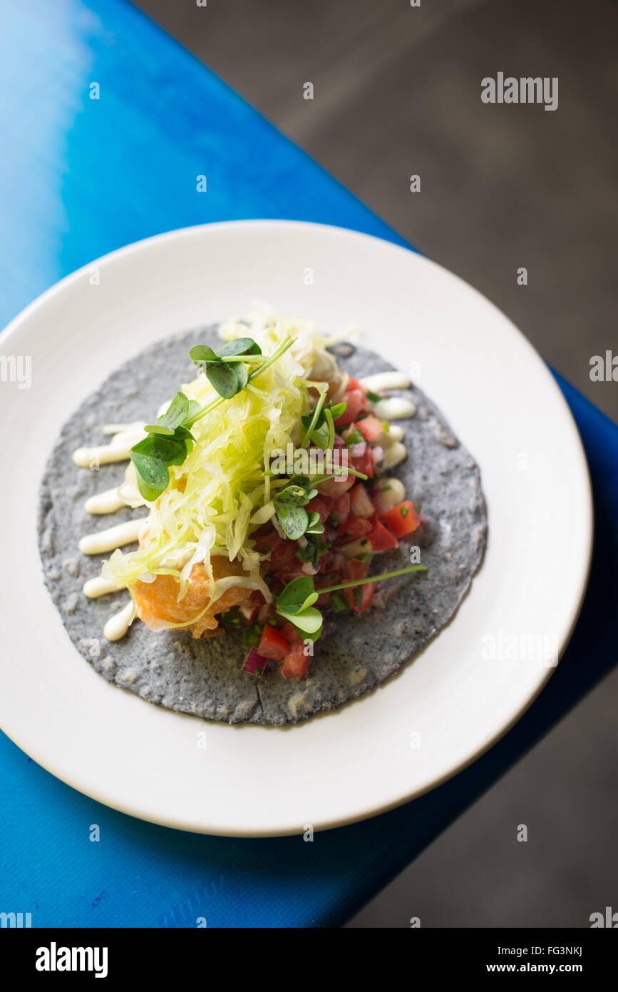 Un pesce taco con decorazione su un blu tortilla di mais sull'angolo di un blu brillante tabella. Foto Stock