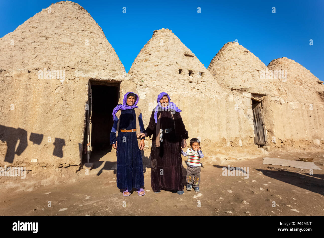 Due donne e un bambino in piedi fuori dalla porta di una primitiva abitazione; Harran, Turchia Foto Stock