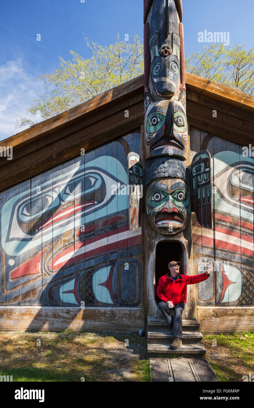 Uomo si siede sui gradini di un clan Tlingit house con smart phone, Totem Bight stato storico Park, Ketchikan, a sud-est di Alaska, STATI UNITI D'AMERICA, molla Foto Stock