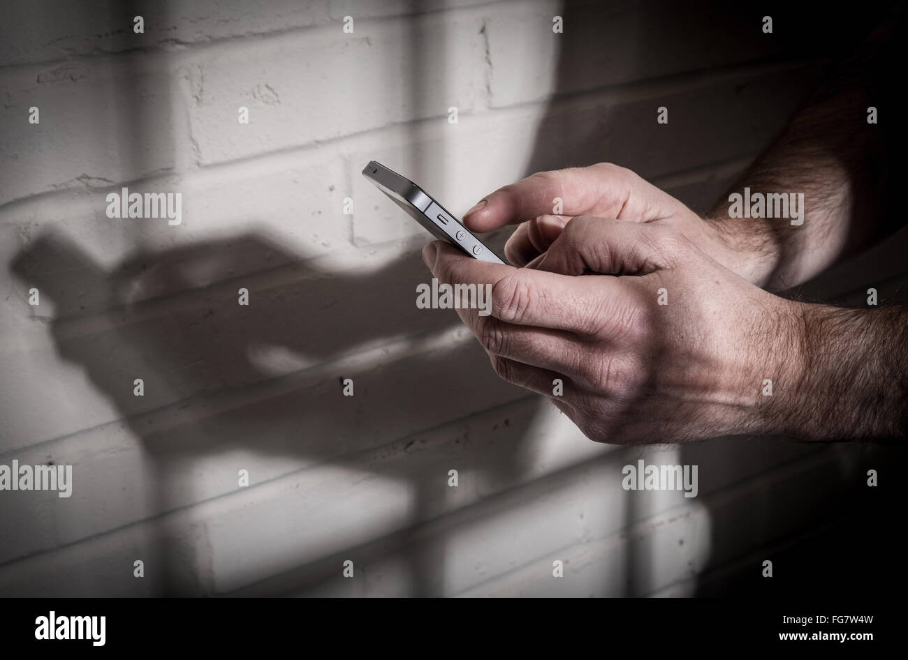 Un detenuto in prigione utilizzando un telefono mobile dietro le sbarre di una cella Foto Stock