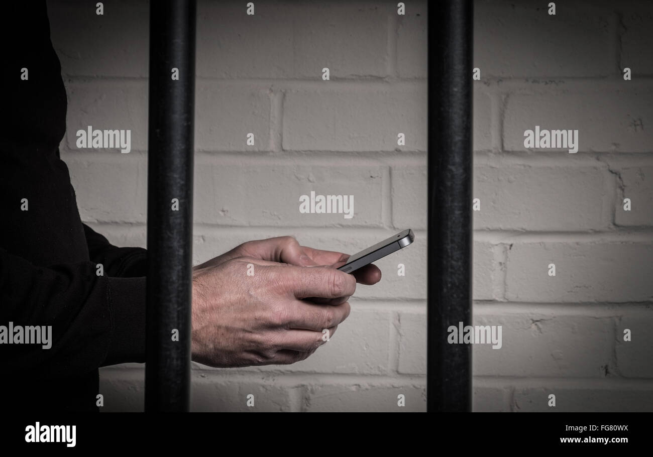 Un detenuto in prigione utilizzando un telefono mobile dietro le sbarre di una cella Foto Stock