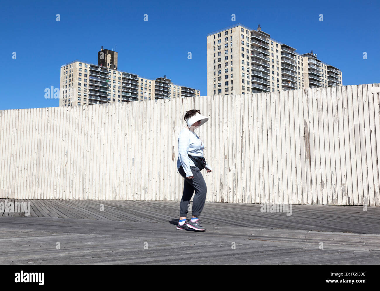 Donna con visiera parasole a Coney island boardwalk con vecchi edifici di appartamenti in background Foto Stock