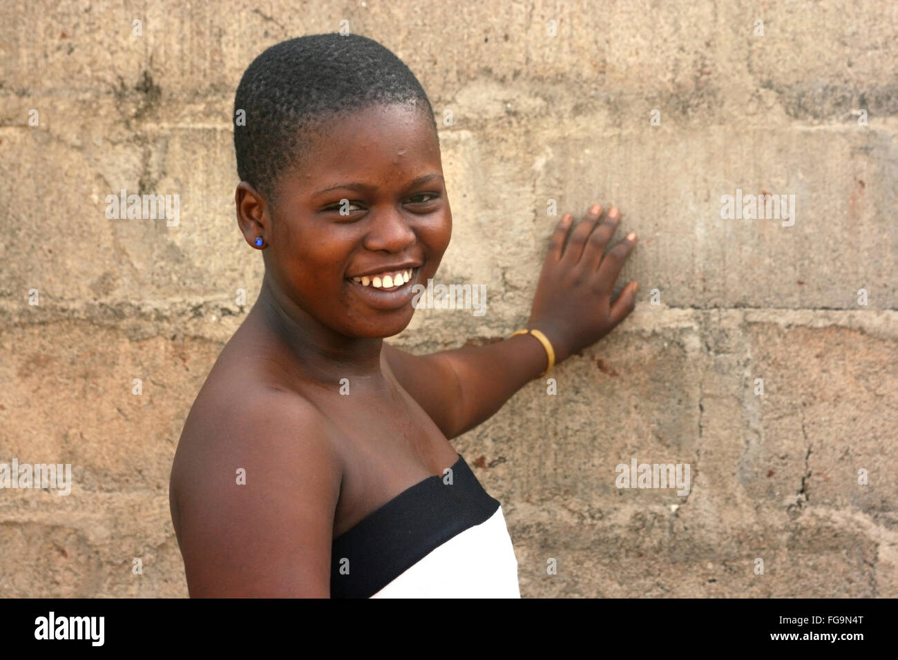 Sorridente ragazza africana si erge da una parete in Benin. Foto Stock