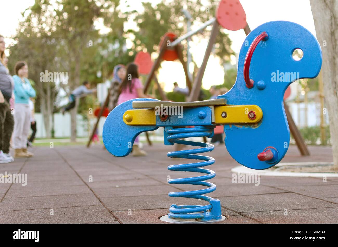 Una vista di un bimbo del parco giochi a dondolo cane giocattolo, sospesi su di una molla e di un piccolo i bambini su altalene sullo sfondo. Concetto di Foto Stock