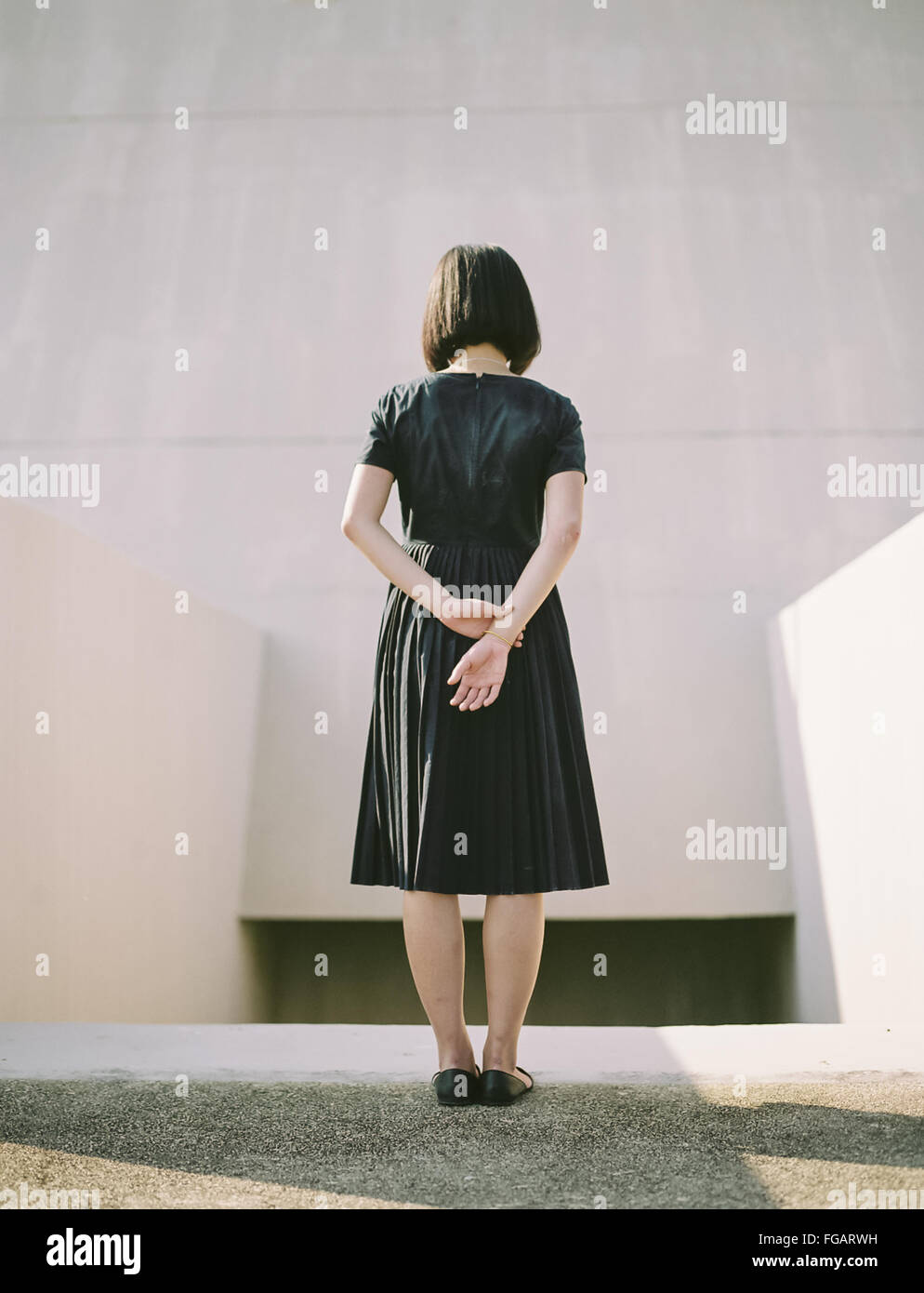 Vista posteriore della donna con le mani dietro la schiena in piedi contro la parete Foto Stock