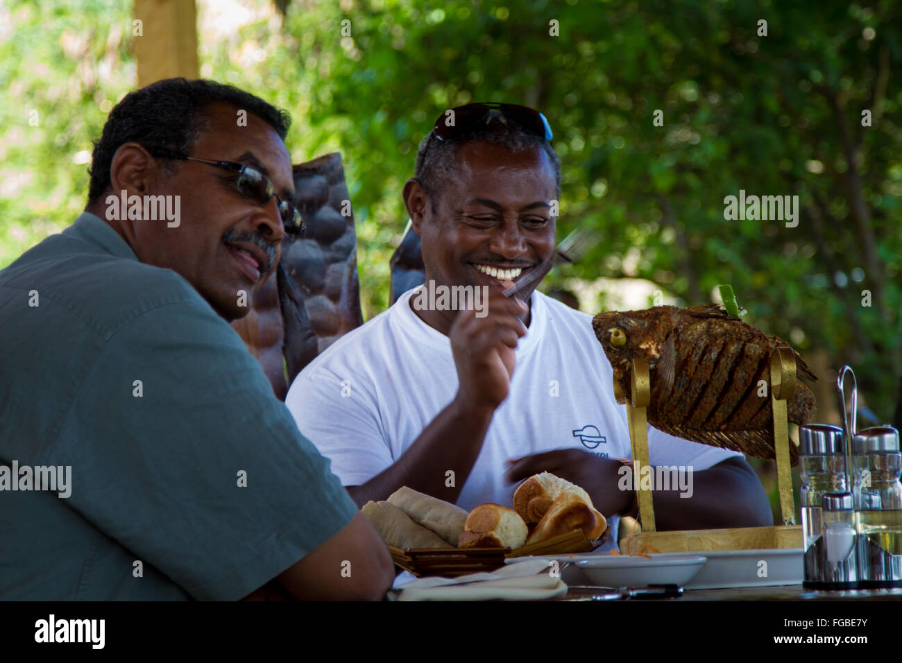 Due uomini godendo un cucinato al momento Tilapia, Etiopia. Foto Stock