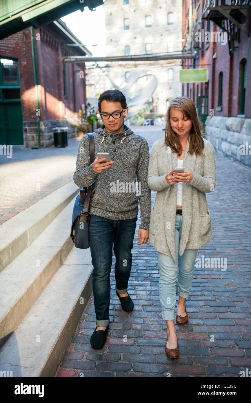 Due giovani cercando in smartphone mentre si cammina sulla strada di città Foto Stock