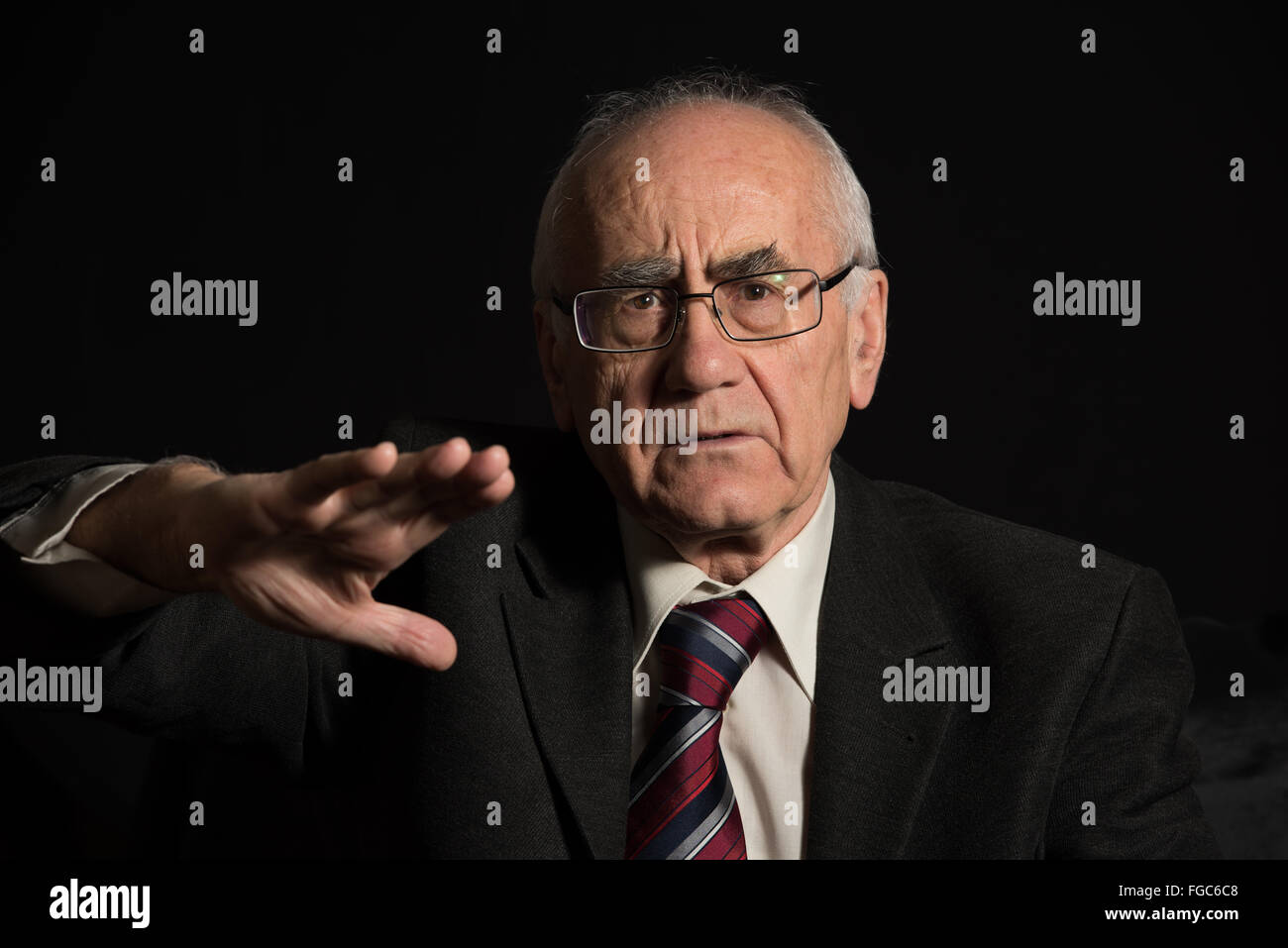 I vecchi proprietari, indossando occhiali su sfondo nero sta discutendo e si articola con la sua mano Foto Stock I vecchi proprietari, indossando occhiali su sfondo nero sta discutendo e si articola con la sua mano Foto Stock