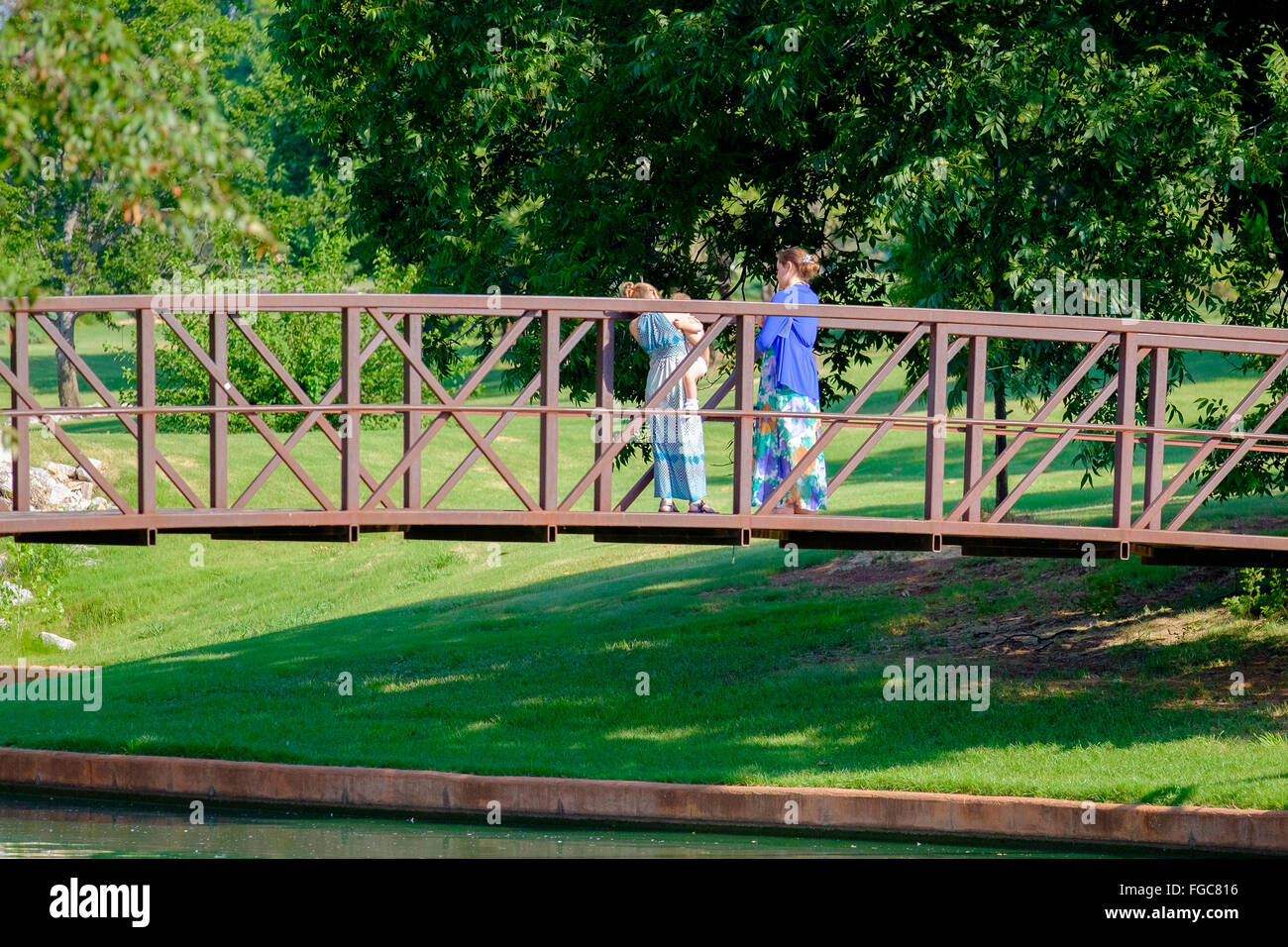 Due giovani donne caucasiche e un bambino si trovano su un ponte a traliccio in metallo in un parco pubblico di Oklahoma City. Oklahoma, Stati Uniti. Foto Stock