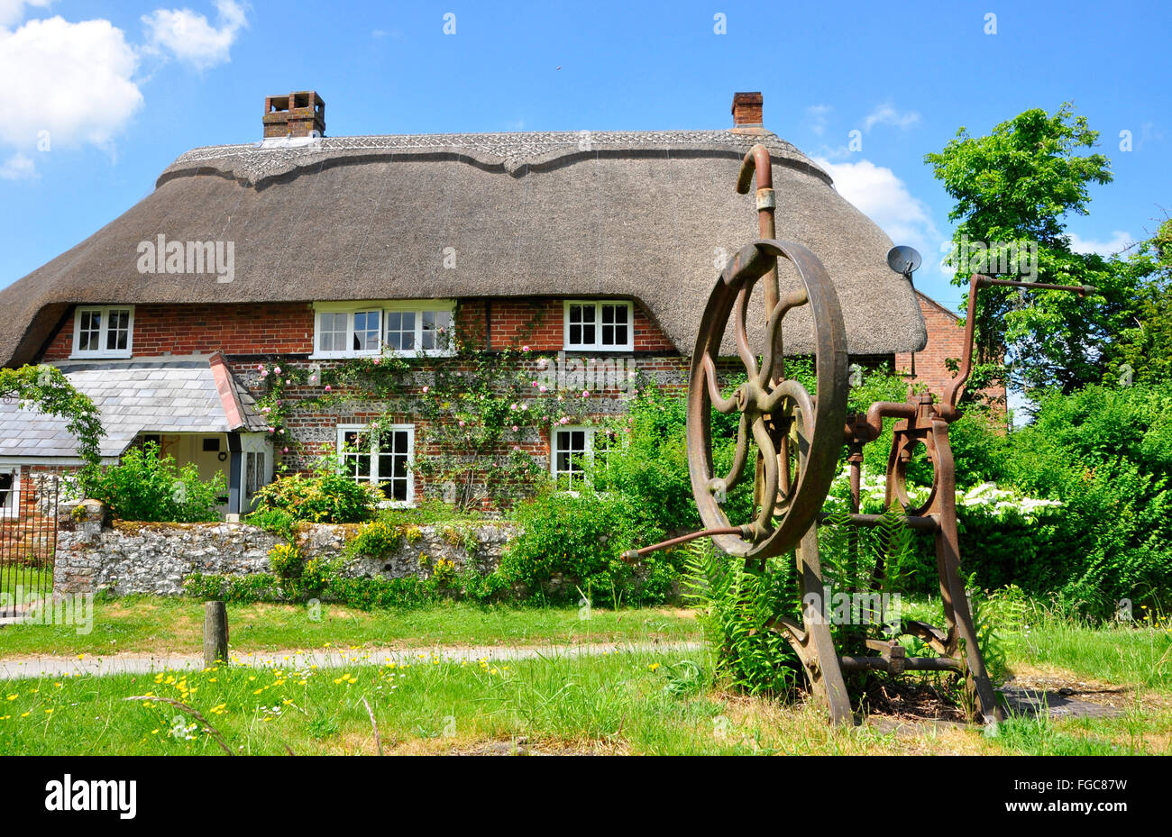 Pompa del villaggio vecchio sul verde villaggio con un cottage di paglia sullo sfondo nel villaggio di Martin , Hampshire, Regno Unito Foto Stock