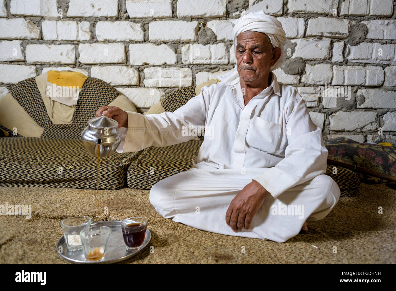 Il vecchio uomo egiziano seduto sul pavimento versando il tè per i suoi ospiti. Foto Stock