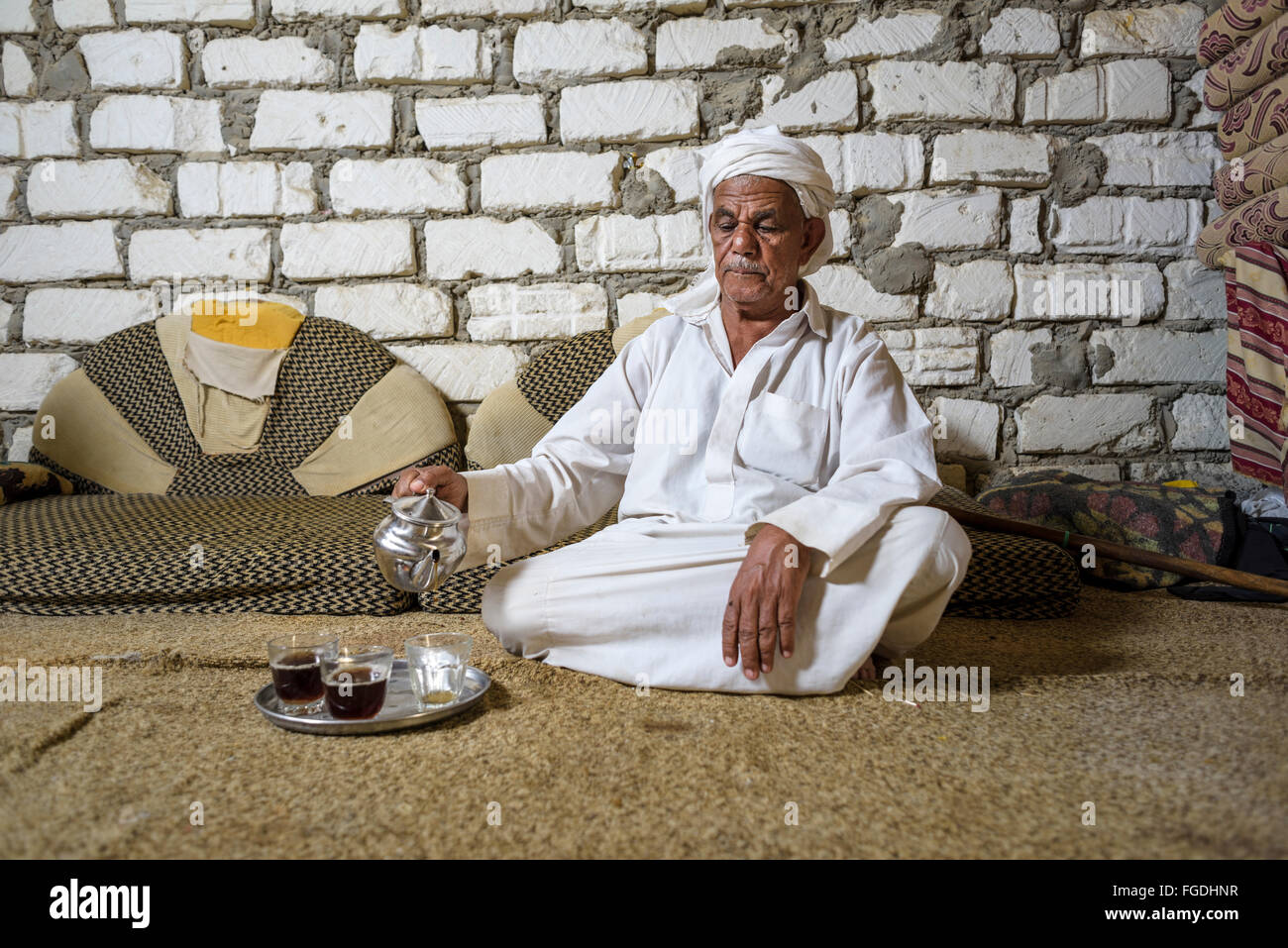 Il vecchio uomo egiziano seduto sul pavimento versando il tè per i suoi ospiti. Foto Stock